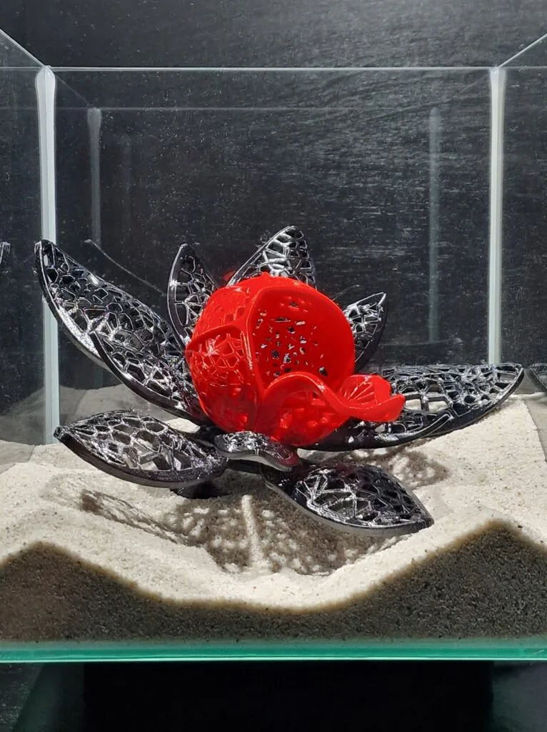 Detailed close-up of the elegant betta fish cave by Aquireef, showcasing its intricate lotus flower design with a striking red center and decorative black petals, placed on a sandy aquarium substrate.